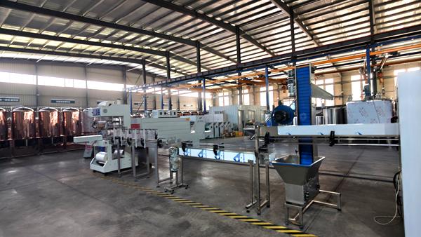 Complete liquid soap bottling line in factory workshop, including filling, capping, labeling and shrink wrapping equipment for liquid detergent
